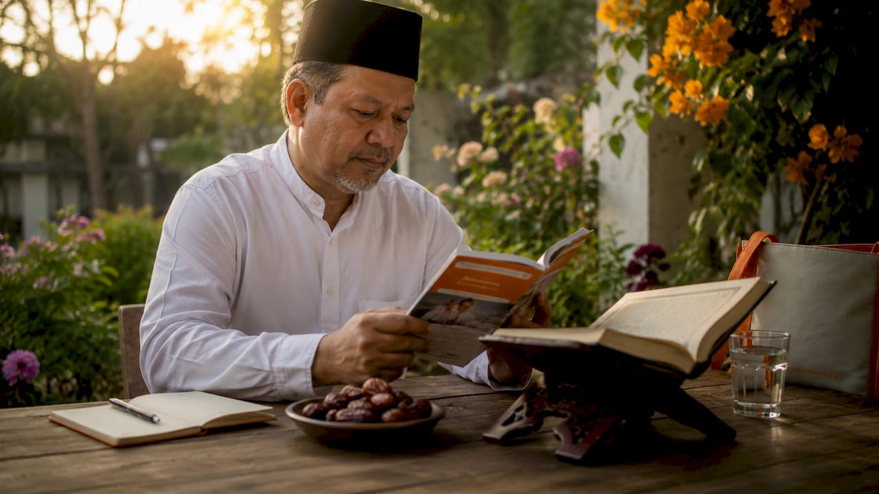 Muslim man reading Islamic charity booklet at home study